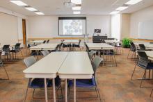 Classroom with desks and chairs in small "T" shaped groups facing a podium.