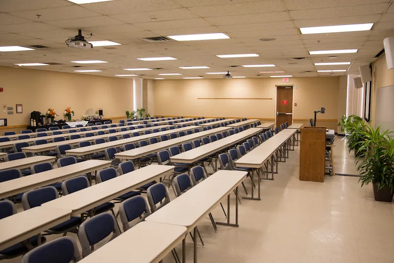 Large room with rows of tables and chairs facing a podium.