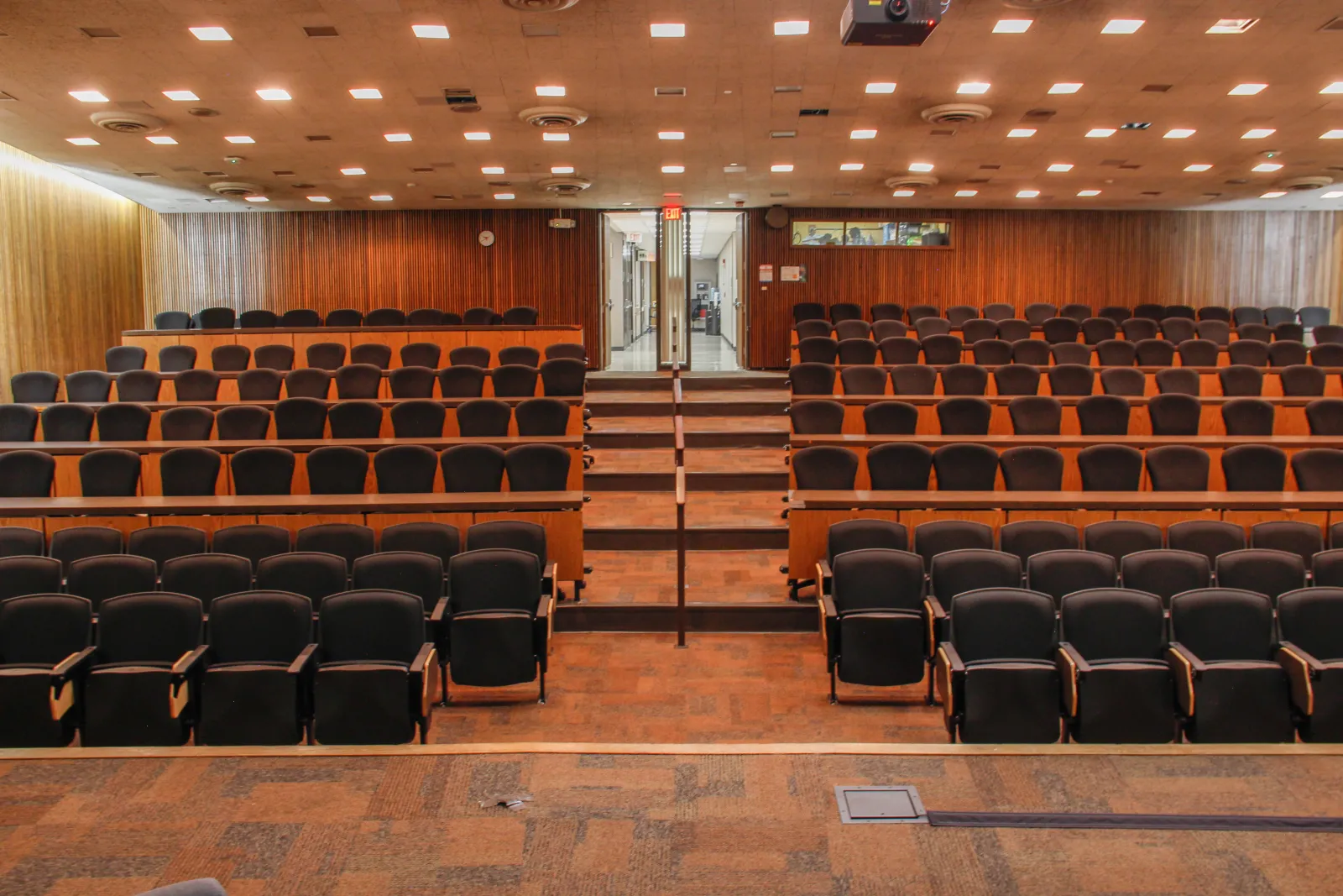 Lecture hall with rows of chars and tables facing a podium.