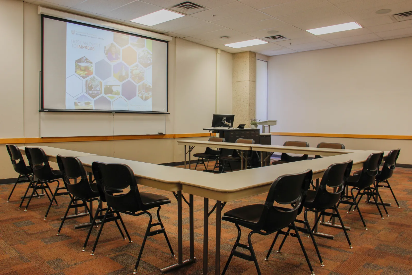 Rows of tables and chairs placed at an angle facing a desk with a podium and a whiteboard.