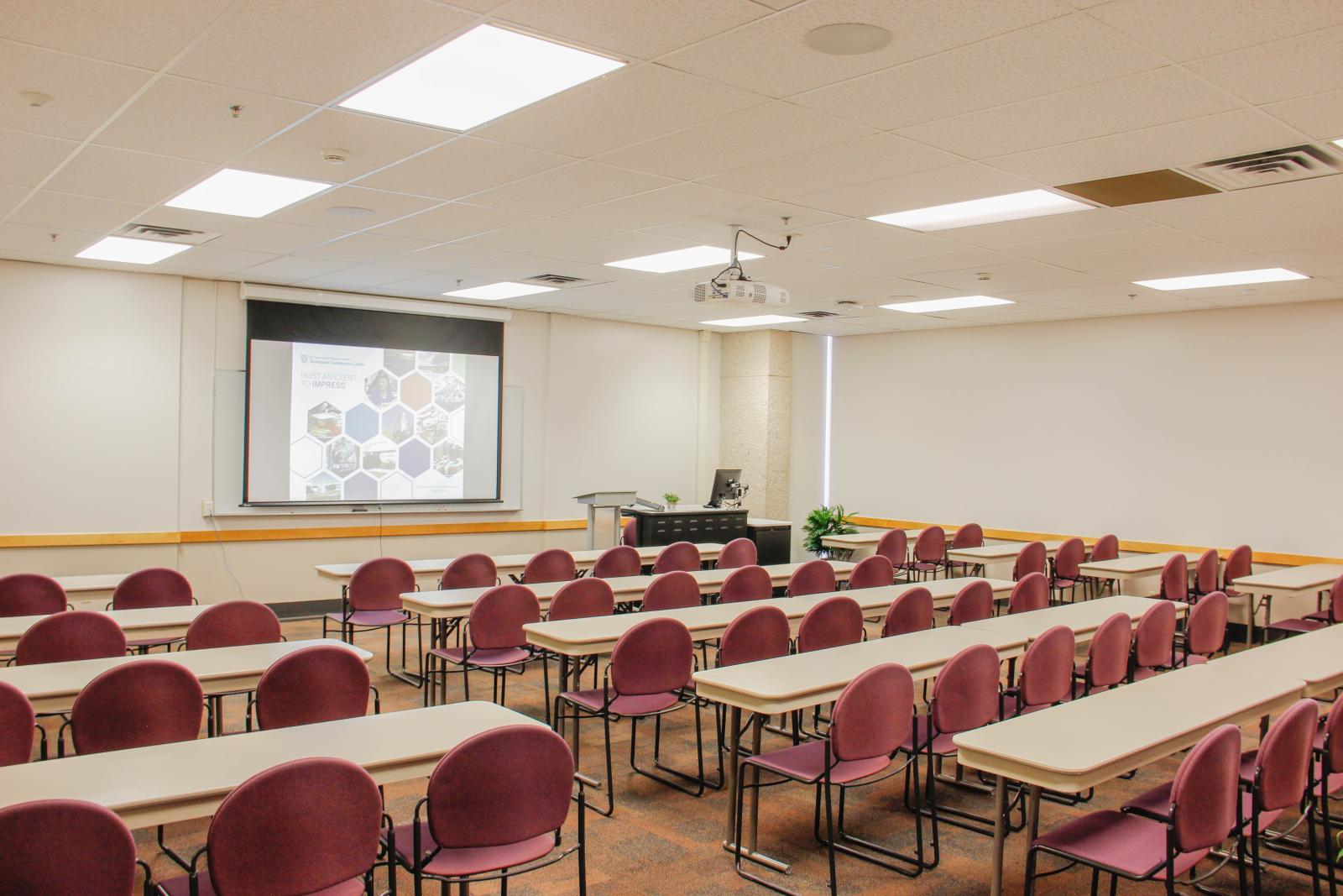 Tables and chairs set up in a "U" shape facing a desk with a podium.